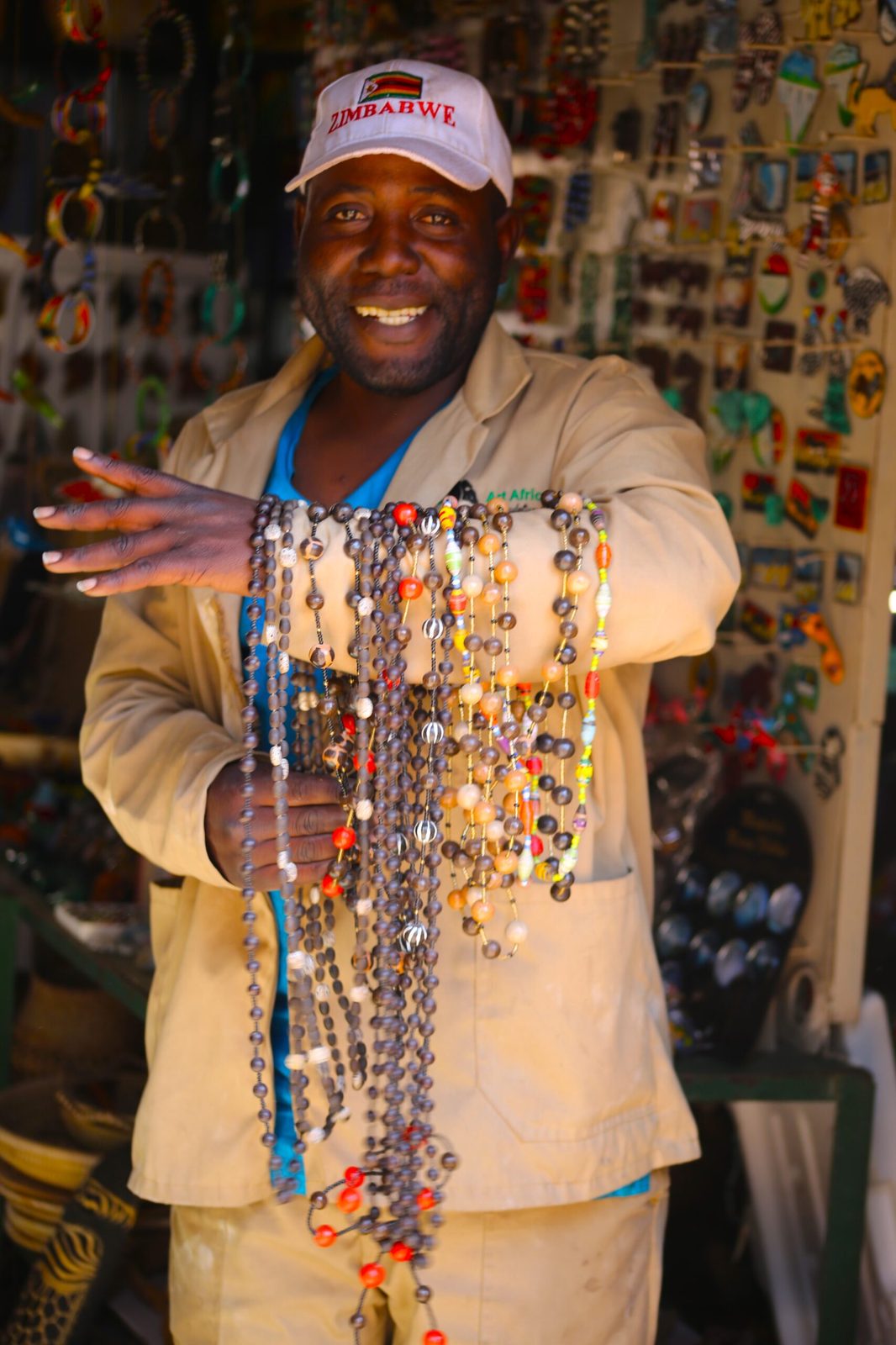 A shopkeeper in a Zimbabwe cap holding out strings of beadwork