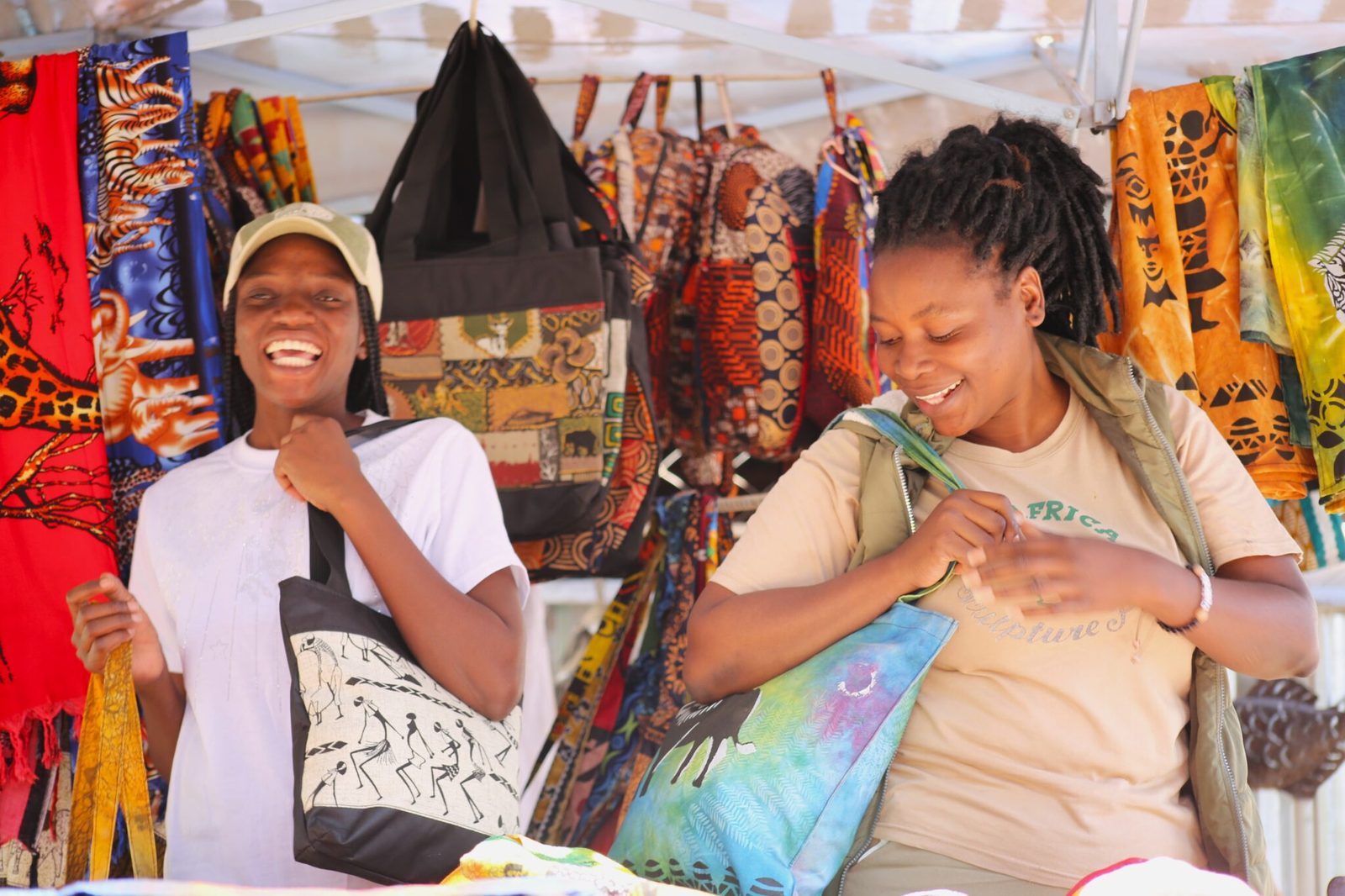 Two visitors laughing as they try printed cotton tote bags